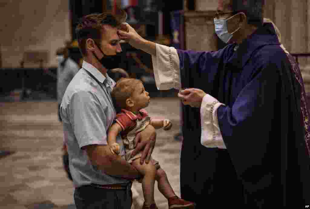 Un hombre con una máscara carga a su hijo para recibir las cenizas durante la Misa en celebración del Miércoles de Ceniza en La Habana, Cuba.