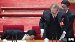 El presidente de China, Hu Jintao (i), guarda sus documentos en un cajón mientras un asistente ayuda a levantarse al expresidente Jiang Zemin tras la clausura del XVIII Congreso del PCCh.